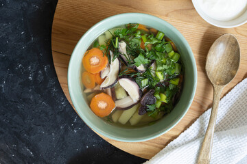 Soup with fresh white mushrooms and potato - traditional dish of russian cuisine in a clay bowl over dark wooden background.Top view with copy space.