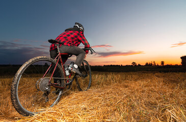 Fototapeta na wymiar A cyclist on a gravel bike stands in a field against the backdrop of the sunset. Low angle view.