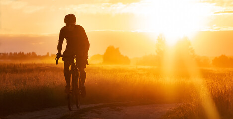 Silhouette of a cyclist riding a trail in a field on a dramatic sunset background.