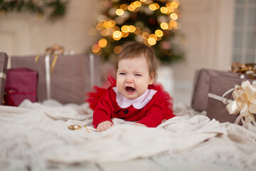 Portrait of crying little girl in red knitted sweater with Christmas present box near Christmas tree