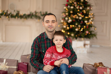 Obraz na płótnie Canvas Smiling father hug his son at Christmas tree, surrrounded presents. Happy family holidays.