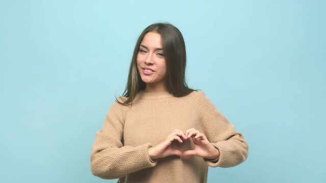 Young cute woman smiling and showing a heart shape with hands