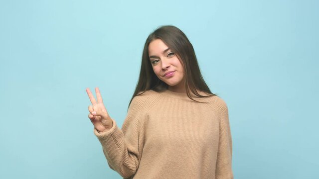 Young cute woman joyful and carefree showing a peace symbol with fingers