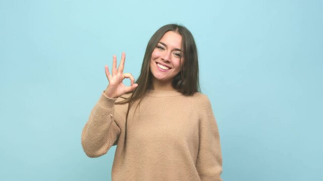 Young cute woman winks an eye and holds an okay gesture with hand