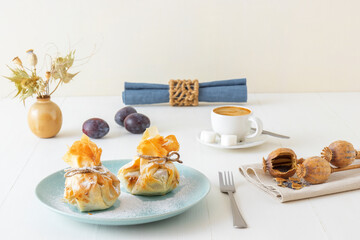 Plum and poppy seeds phyllo purses on a white wooden, delicious vegetarian dessert on a white wooden table.