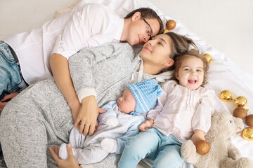 Beautiful family: mom, dad, daughter and newborn son lie in bed embracing on a Christmas day among the decorations and garlands
