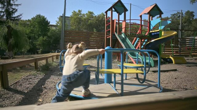 Little cute blond girl spinning on a merry go round at playground