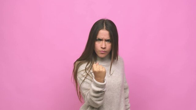 Young cute woman showing fist to camera, aggressive facial expression
