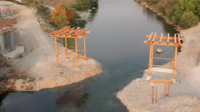 Bridge construction: metal scaffolding used as temporary support for the deck of a small pedestrian bridge. Pair of iron frames on the banks of a narrow river. 