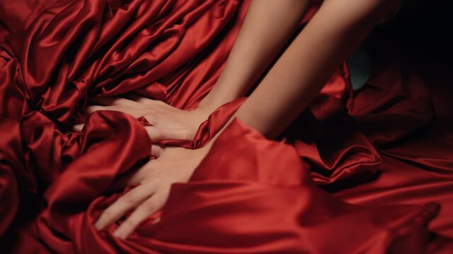 Woman hands holding red satin sheet on bed. Unknown girl having moment pleasure.