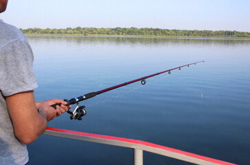 close-up of male hands of a young man holding a fishing rod leaning on a railing on the river bank in the morning. The theme of fishing, recreation, leisure, outdoor activities
