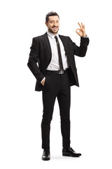 Full length portrait of a young man wearing black suit and gesturing ok sign
