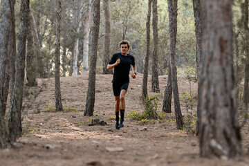Obraz premium Atleta joven corriendo por un bosque, vestido con una camiseta negra y pantalón corto negro