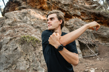 Atleta joven mirando hacia la izquierda estirando los hombros en el bosque 