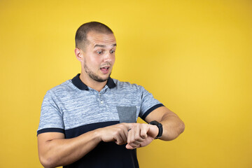 Russian man standing over insolated yellow background surprised and pointing his watch because it's...
