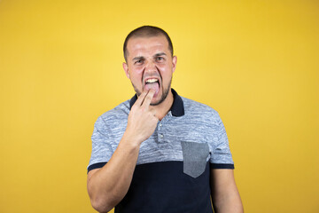 Russian man standing over insolated yellow background disgusted with her hand inside her mouth