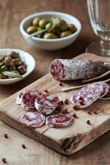 Sliced french salami with fresh rosemary and olives on rustic wooden background.	