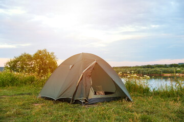 green tourist tent is on the bank of the river at sunset