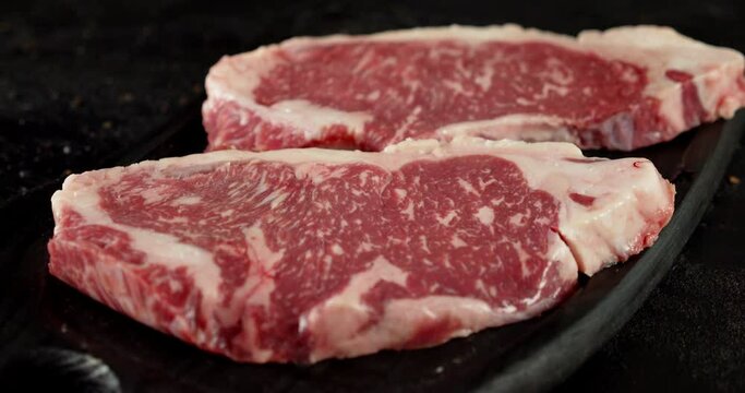 Raw beef striploin steak on a cutting board rotates. 
