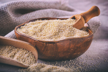 Amaranth grits in a wooden bowl with scoop on the background of burlap, closeup with selective focus