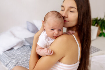 Young beautiful brunette mom holds a newborn baby in her arms

