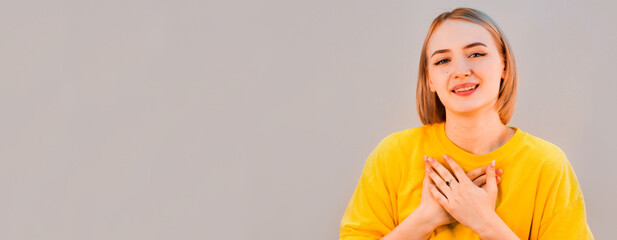 Beautiful positive friendly-looking young european girl with lovely sincere smile feeling thankful and grateful, showing her heart filled with love and gratitude holding hands on her breast