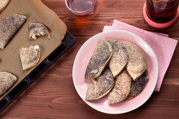 Traditional Russian sweet shortcrust pastry with quark or cottage cheese and raisins, sochni or sochniki pies or pirozhki with poppy seeds on pink plate with tea in the morning on brown wooden table