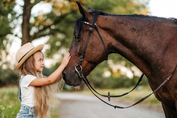 Friendship of a child with a horse. A little girl is affectionately stroking her horse. Walking...