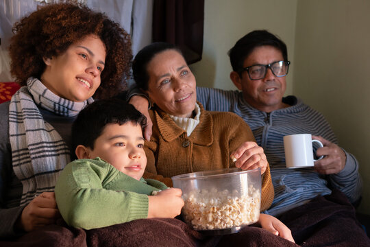 Happy Latin Multigenerational Family Sitting In Couch Watching Movies Inside The House In Living Room. Unity, Happiness, Affection, Love, Care Concept.