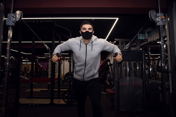 Fototapeta na wymiar Muscular man workout in gym doing exercises for chest, cable crossover. Strong male in medical mask