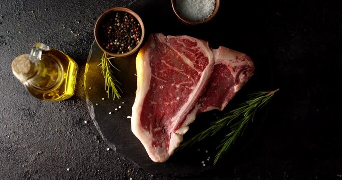 Raw steak beef t-bone on stone board rotates with rosemary. 