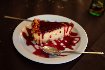 Creamy piece of cheesecake with its cutlery on top of a plate on the table.