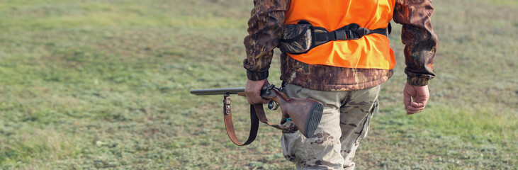 Hunter man in rural field with shotgun and backpack during hunting season