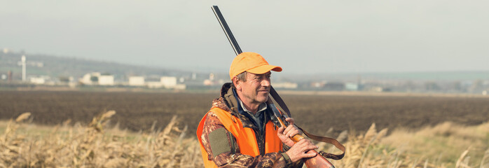 Hunter man in rural field with shotgun and backpack during hunting season