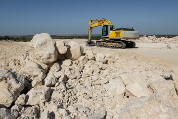 A large yellow tracked excavator is mining rock in a quarry.