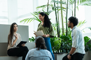 Confident brazilian female boss with tablet talking to business team at metting in open office space. Unity, teamwork, collaboration concept..