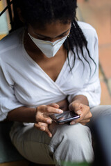 Fototapeta na wymiar Young black woman in face mask using a smartphone