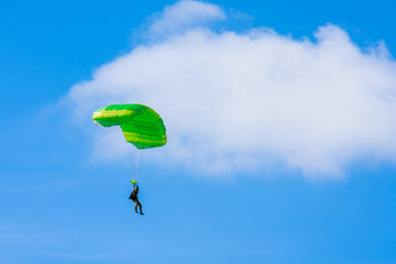 A parachutist with a light green parachute canopy against a background of blue sky and white clouds. Skydiving.