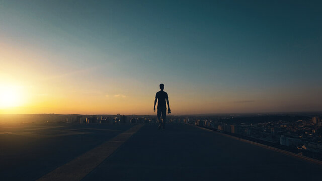 Silhouette Of A Man Walking On Top Of The Building At Sunset And Cloudy Sky. Concept  Photographer Man Image.