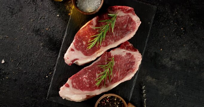 Steak striploin raw beef with rosemary and spices rotates.