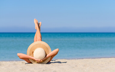 A girl in a straw hat with her legs upside down is sunbathing on the beach. Vacation concept by the sea.