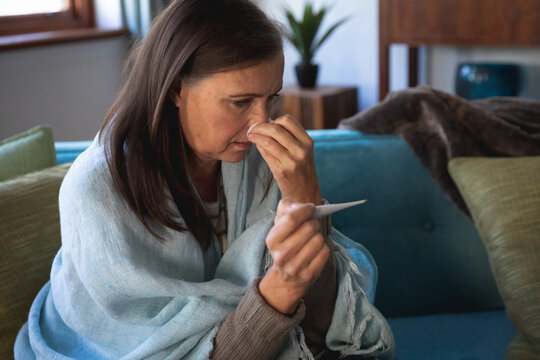 Sick woman holding her nose while measuring her temperature