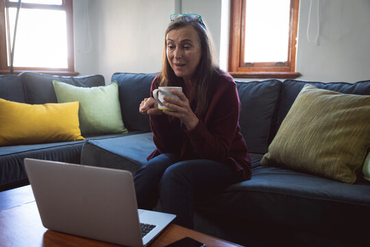 Woman holding coffee cup while having a video call on laptop at home