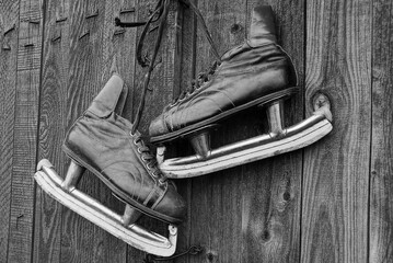 a pair of old skates with black leather boots and white blades hang on a gray wooden wall