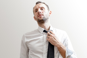 tired young man in white shirt takes off his tie on gray background