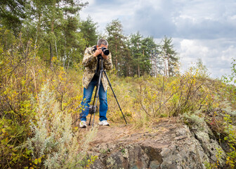 Man photographing autumn mountain landscape with a camera on a tripod