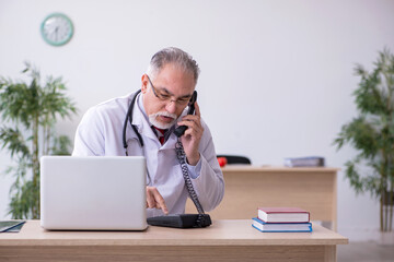Naklejka premium Old male doctor working in the clinic