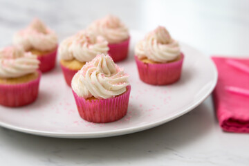 Close Up of Vanilla Cupcakes with Vanilla Icing in Pink Paper Cups with Pink Sprinkles on a White Plate on White Countertop with Pink Napkin Beside