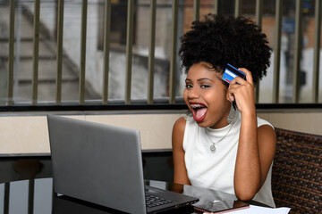 a teenage girl shopping online, holding a credit card next to a laptop on her desk