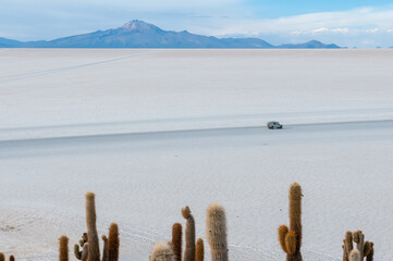 Landscape of the crystallized Bolivia salt flat with a car driving through.